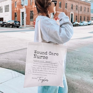 May include: A white tote bag with black text that reads "Wound Care Nurse" and a definition of the term. The bag also includes the name "Taylor" at the bottom.