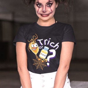 以下が含まれることがあります： ハロウィーンをテーマにしたグラフィックの黒いTシャツ。デザインには、漫画の細菌、"Treat"と書かれた薬瓶、疑問符、"Trich or Treat"という言葉が含まれています。クモの巣もデザインの一部です。