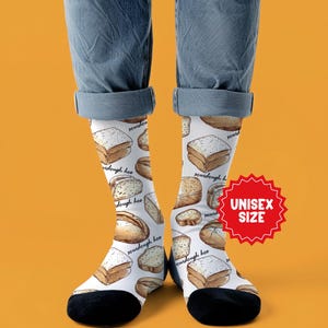 May include: White socks with a repeating pattern of various bread loaves and slices, including sourdough. The socks have black heels and toes, and the text "sourdough hoe" is written on the socks. A red starburst graphic reads "UNISEX SIZE".