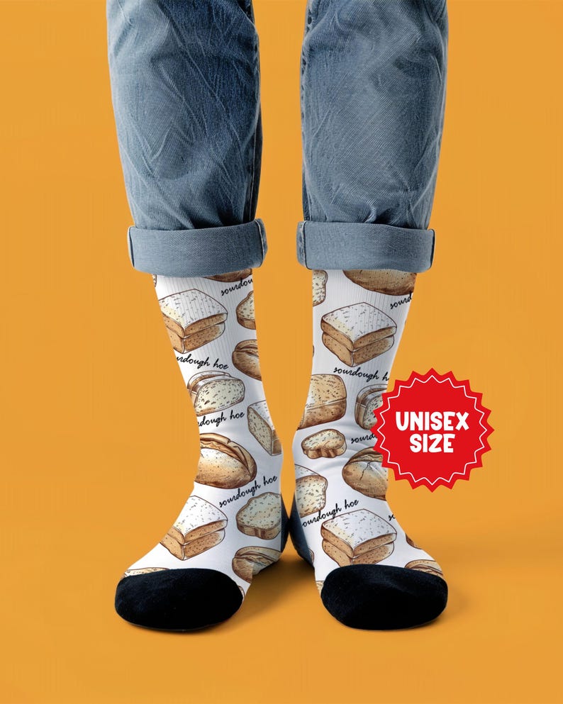 May include: White socks with a repeating pattern of various bread loaves and slices, including sourdough. The socks have black heels and toes, and the text "sourdough hoe" is written on the socks. A red starburst graphic reads "UNISEX SIZE".