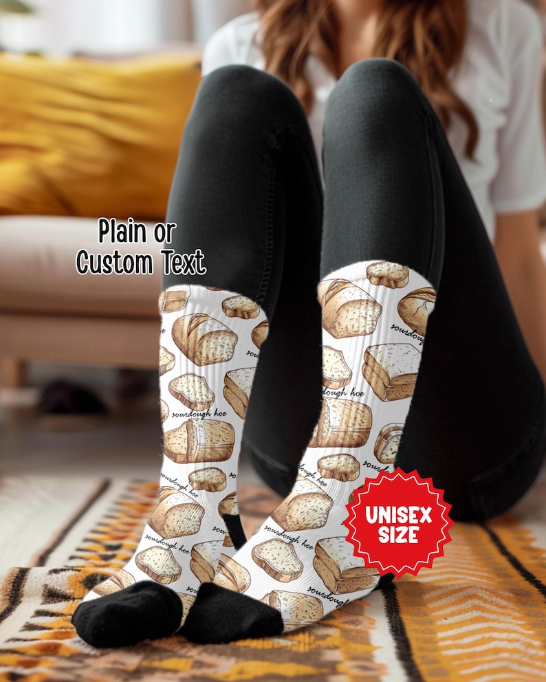 May include: White socks with a repeating pattern of illustrated sourdough bread loaves. The socks have black heels and toes. Text on the socks reads "sourdough hoo". A red badge reads "UNISEX SIZE". The text "Plain or Custom Text" is also visible.