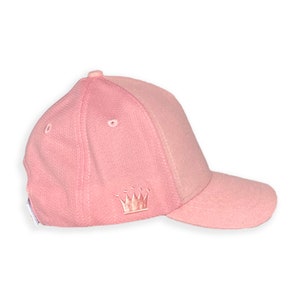 May include: A pink baseball cap with a small embroidered crown on the front.