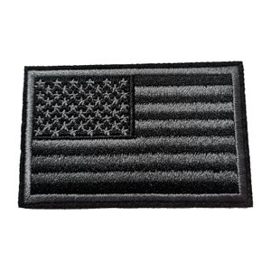 May include: A rectangular, embroidered patch depicting the American flag in shades of grey. The flag's stars and stripes are clearly defined, with a black border. The patch is designed for application on clothing or accessories.