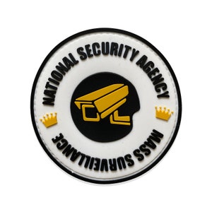 Può includere: Toppa rotonda bianca con testo nero che recita "National Security Agency Mass Surveillance" con un'icona di telecamera di sorveglianza nera e gialla e due icone di corona gialle.