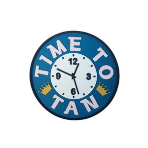 May include: A blue round patch with the words "TIME TO TAN" in pink letters around a white clock face with black hands. The clock face has black numbers and two gold crowns on either side of the clock face.