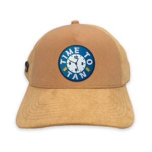 Puede incluir: Una gorra de béisbol de gamuza marrón con un parche azul y blanco que dice "TIME TO TAN" con una esfera de reloj y dos coronas.