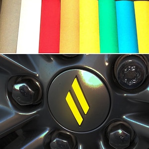 May include: Close-up of a black car wheel with a yellow and black logo in the center. The logo is a stylized letter "M" with two parallel lines.