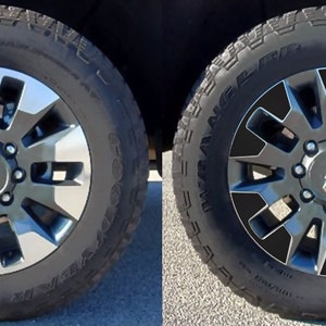 May include: Two images of a black truck wheel with a silver rim. The wheel on the left has a silver center cap, while the wheel on the right has a black center cap.