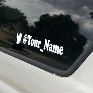 May include: A white vinyl sticker with a Twitter bird icon and the text "@Your_Name" on a black car window.
