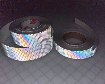 Könnte beinhalten: Zwei Rollen silbernes reflektierendes Klebeband mit einem regenbogenfarbenen, irisierenden Finish. Das Klebeband hat ein Diamantenmuster.