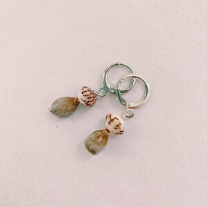 May include: A pair of silver hoop earrings with a brown and white shell pendant on each earring.