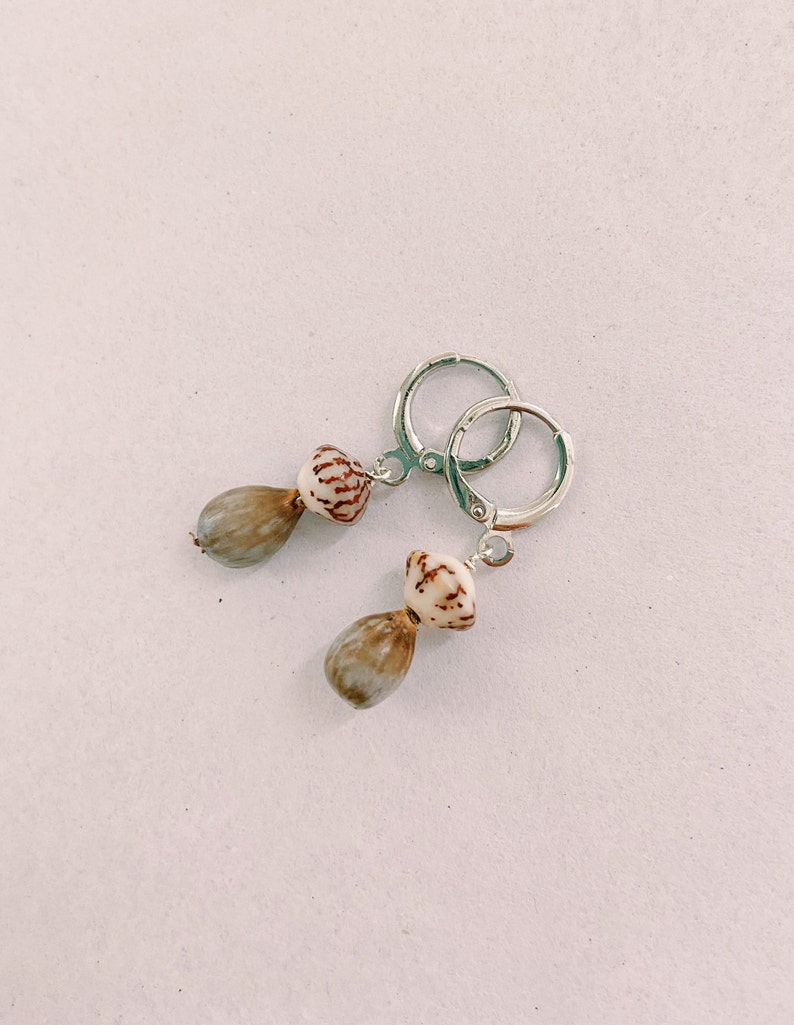 May include: A pair of silver hoop earrings with a brown and white shell pendant on each earring.