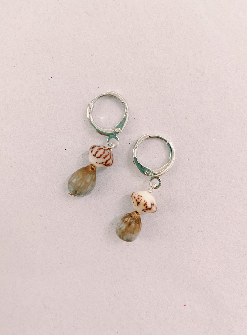 May include: A pair of silver hoop earrings with a brown and white shell charm hanging from each hoop.