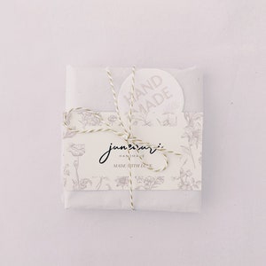 May include: A white paper package tied with twine and a floral design. The package has a sticker that says "HAND MADE" and a label that says "june + mari HANDMADE MADE WITH LOVE".