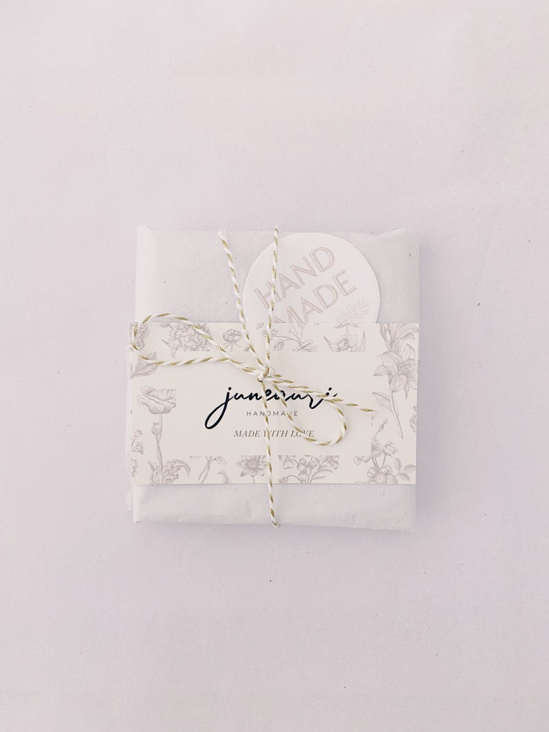 May include: A white paper package tied with twine and a floral design. The package has a sticker that says "HAND MADE" and a label that says "june + mari HANDMADE MADE WITH LOVE".