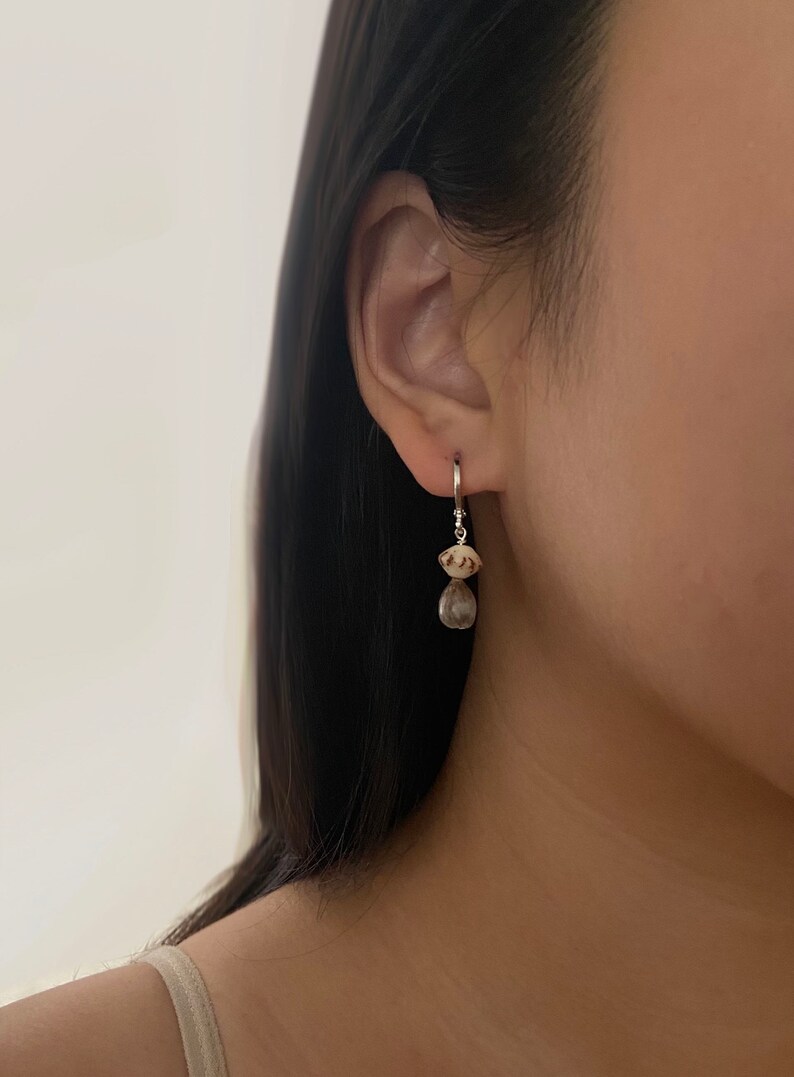 May include: A pair of silver hoop earrings with a small white and brown seashell charm hanging from each hoop.