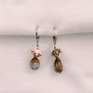 May include: A pair of silver hoop earrings with two brown and white seed pods dangling from each hoop.