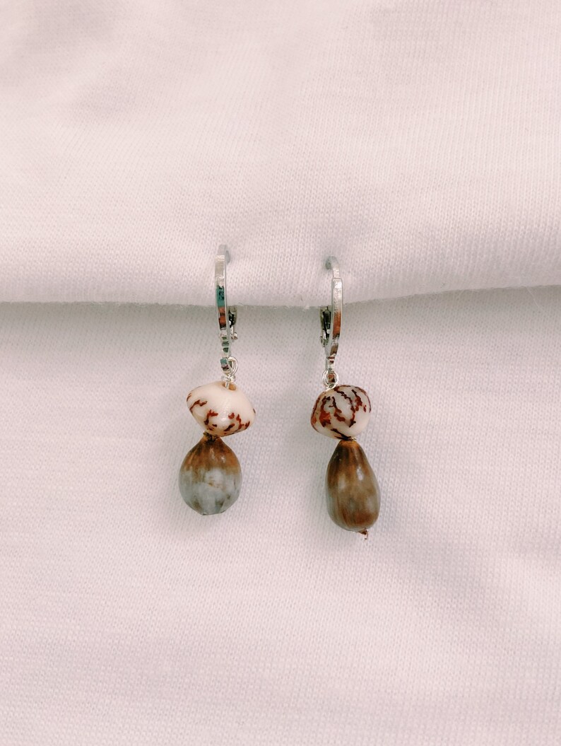 May include: A pair of silver hoop earrings with two brown and white seed pods dangling from each hoop.