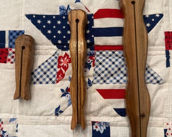 May include: Three wooden clothespins of varying lengths arranged vertically. Each pin features a smooth, polished brown finish with a central slit running down the length of the body and a small circular hole near the top end of the wooden structure.