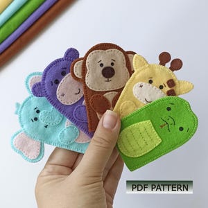 May include: A set of five felt finger puppets featuring animal designs including a light blue elephant, a purple hippo, a brown monkey, a yellow giraffe, and a green frog, with the text PDF PATTERN visible in the lower right corner.