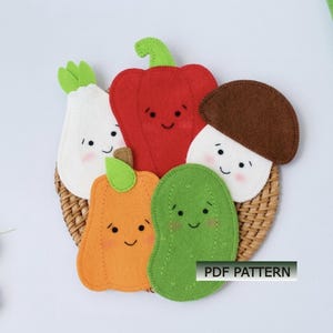 May include: A felt craft featuring a red bell pepper, white radish, orange pumpkin, green cucumber, and brown mushroom, each with a smiling face. The vegetables are arranged on a woven basket. The text "PDF PATTERN" is visible.