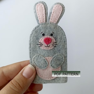 Op de afbeelding: Een grijze vingerpop van vilt in de vorm van een konijn met lange oren, een lichtroze neus en een lichtroze buikvlek. De pop heeft gestikte details waaronder ogen, snorharen en een mond. De tekst PDF PATTERN is zichtbaar.
