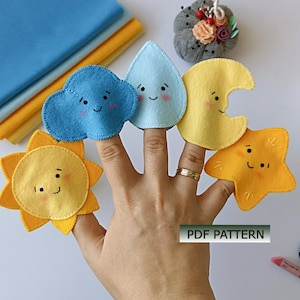 May include: Five felt finger puppets featuring weather-themed designs including a yellow sun, a blue cloud, a light blue raindrop, a yellow crescent moon, and a yellow star. Each puppet has a stitched face with pink cheeks. Text reads PDF PATTERN.