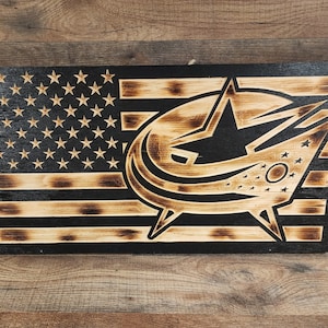May include: A wooden American flag with a black and brown wood-burned design of the Carolina Hurricanes hockey team logo.