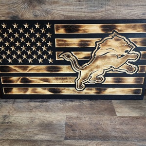 May include: A wooden American flag with a burnt wood finish. The flag has a lion logo in the center.