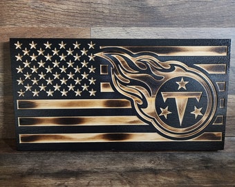 May include: A wooden American flag with a burnt effect, featuring the Tennessee Titans logo in the lower right corner. The logo is a circle with a flame design and the team's 'T' inside.