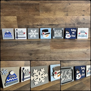 May include: A set of 10 wooden winter-themed signs with various designs, including snowflakes, snowmen, hats, and phrases like "Let it snow" and "Baby it's cold".