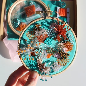 May include: A turquoise embroidery hoop with a beaded design of coral and sea life. The beads are in shades of orange, white, and teal.