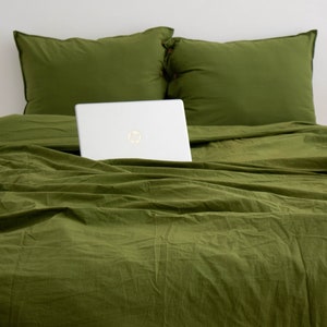 May include: A green duvet cover with a laptop computer partially hidden under it. The duvet cover is on a bed with two green pillowcases.