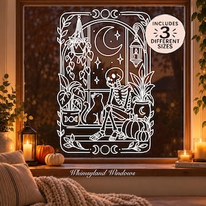 May include: A white line art window decal featuring a skeleton sitting with a cat, a hanging plant, a lantern, and pumpkins. The design includes a crescent moon and stars. A circular badge in the corner states: INCLUDES 3 DIFFERENT SIZES.
