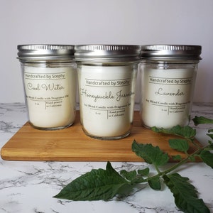 May include: Three glass candle jars with silver lids. The labels read "Handcrafted by Stephy" and list the scents "Cool Water", "Honeysuckle Jasmine", and "Lavender". Each jar is labeled as a soy blend candle with fragrance oil and states "Hand poured in California".