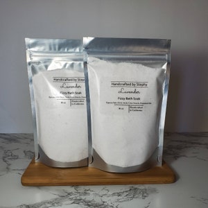 Puede incluir: Dos bolsas plateadas de baño efervescente con aroma a lavanda, cada una con 10 onzas de producto. Las bolsas están etiquetadas con "Handcrafted by Step/Stephy Lavender Fizzy Bath Soak" y "Handcrafted in California".