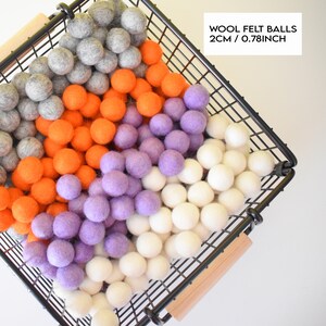 May include: A black wire basket filled with colourful wool felt balls. The balls are in shades of grey, orange, purple, and white. The text "WOOL FELT BALLS 2cm / 0.78inch" is displayed in a white rectangle.