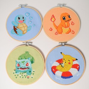 K&ouml;nnte beinhalten: Vier bestickte Reifen mit verschiedenen Pok&eacute;mon-Charakteren. Die Reifen sind aus Holz und haben eine hellbraune Farbe. Der erste Reifen zeigt Squirtle, der zweite Charmander, der dritte Bulbasaur und der vierte Pikachu.