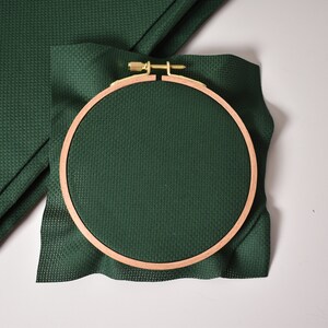 Op de afbeelding: Een groene Aida-stof is gespannen in een houten borduurring. De ring heeft een diameter van 15 cm.