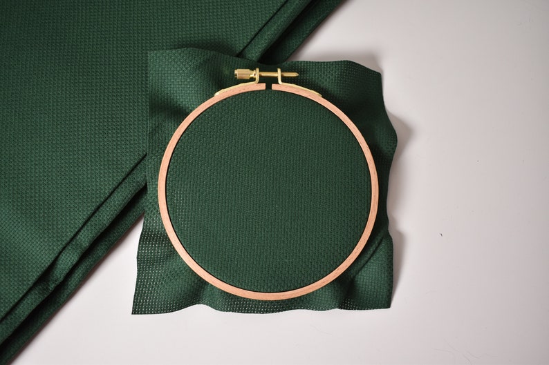Op de afbeelding: Een groene Aida-stof is gespannen in een houten borduurring. De ring heeft een diameter van 15 cm.