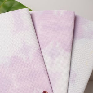 Op de afbeelding: Drie lavendel en witte tie-dye yogamatten op elkaar gestapeld.