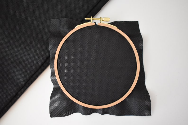 Peut inclure: Un cercle &agrave; broder noir avec un morceau de tissu Aida noir tendu dessus.