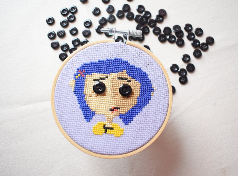 May include: A purple and blue cross-stitch embroidery of a girl with blue hair and yellow shirt. The embroidery is framed in a wooden hoop.