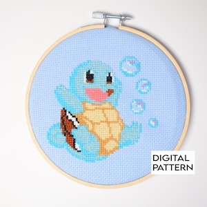 May include: A blue and yellow cross-stitch pattern of Squirtle, a Pokemon character, blowing bubbles on a light blue background. The pattern is framed in a wooden embroidery hoop. The text "DIGITAL PATTERN" is in the lower right corner.