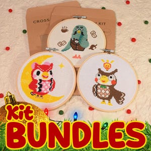 May include: Three cross-stitch kits featuring owl designs. One owl is on a crescent moon, another has a lightbulb, and the third has coffee beans. The kits are in wooden hoops, with brown paper packaging in the background. The word "BUNDLES" is in red.