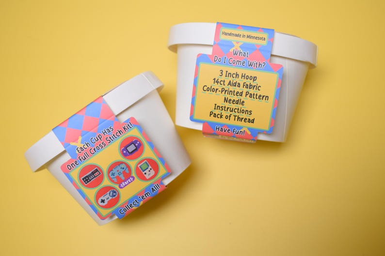 May include: Two white containers with cross-stitch kits. Each kit includes a 3-inch hoop, 14ct Aida fabric, a color-printed pattern, a needle, instructions, and a pack of thread. The kits feature retro video game graphics and the text "Collect 'em All!"