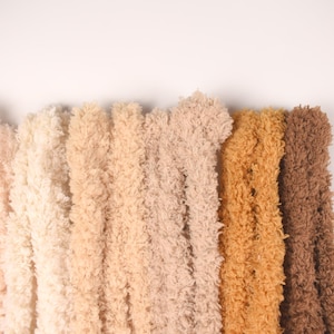 Peut inclure: Gros plan sur plusieurs brins de fil doux de différentes couleurs neutres, dont rose clair, crème, beige, beige clair et marron. Le fil a un aspect doux et texturé, idéal pour les projets de création.