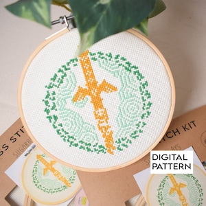 May include: A green and yellow cross stitch pattern in a wooden embroidery hoop. The pattern is a stylized sword with a green and yellow gradient.