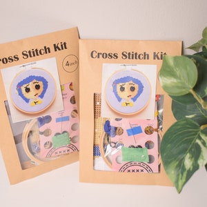 May include: Two brown paper cross stitch kits with a 4 inch hoop featuring a cartoon character with blue hair and a yellow shirt. The kits include embroidery floss, needles, and aida cloth.