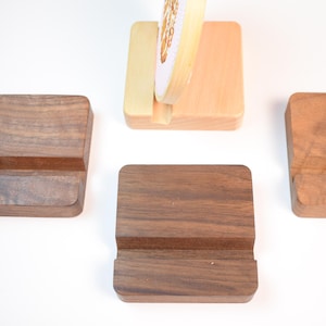 May include: Wooden phone stands in various stages of completion. The stands are made of different types of wood, including a dark walnut and a lighter, natural wood. Each stand has a slot to hold a phone or tablet.